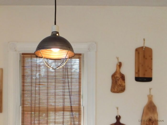 Industrial-looking lamp with a glowing bulb in front of a kitchen window